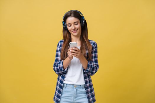 Beautiful young woman in headphones listening to music and dancing on yellow background