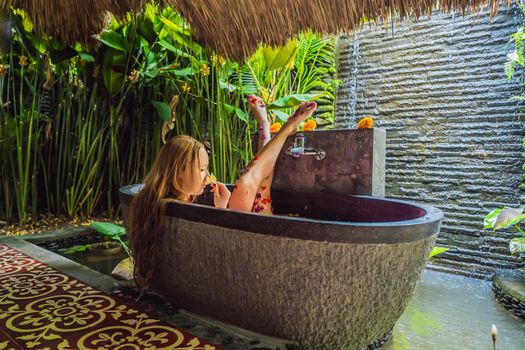 Attractive Young woman in bath with petals of tropical flowers and aroma oils. Spa treatments for skin rejuvenation. Alluring woman in Spa salon. Girl relaxing in bathtub with flower petals. Luxury.