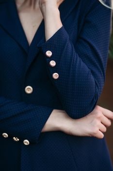 Cropped shot of elegant gorgeous blonde businesswoman in expensive dark black jacket and trousers with golden buttons on sleeves. She is standing with arms crossed.