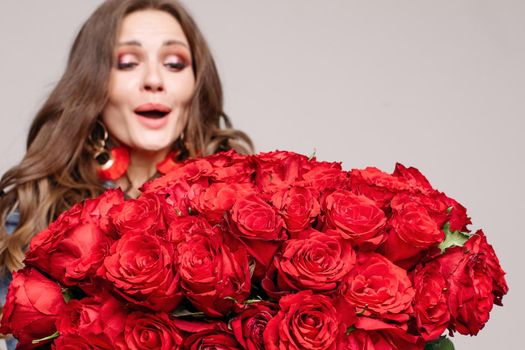 Studio portrait of shocked model with brunette hair and make up looking with astonishment at beautiful big bouquet of roses. Copyspace on white. Isolate. Studio shot.