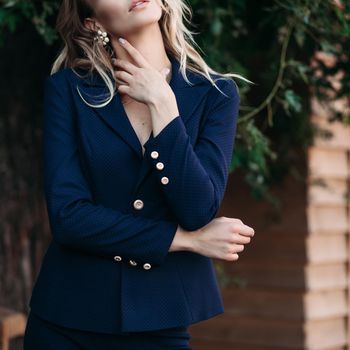 Cropped shot of elegant gorgeous blonde businesswoman in expensive dark black jacket and trousers with golden buttons on sleeves. She is standing with arms crossed.