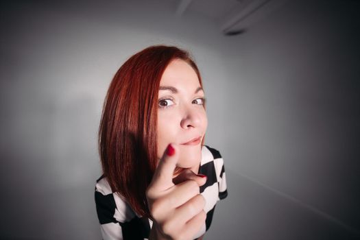 Close up of young pretty lady in black and white blouse looking at camera and holding her finger up. Beautiful woman with red hair and brown eyes looking curiously and wanted to tell idea.