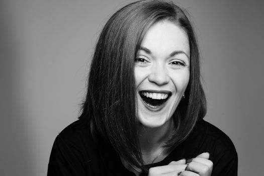 Black and white portrait of gorgeous and charming young woman. Adorable and positive model with white teeth and perfect skin looking at camera and smiling with sincere smile.