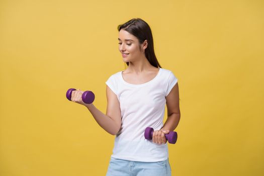 Shot of a beautiful and sporty young woman lifting up weights against yellow background