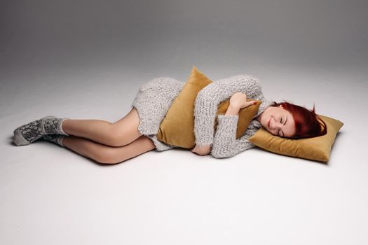 Studio portrait of a woman in a sweater hugging a pillow. The concept of fatigue or odicancy. Isolated on a gray background.