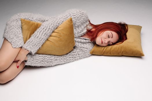 Studio portrait of a woman in a sweater hugging a pillow. The concept of fatigue or odicancy. Isolated on a gray background.