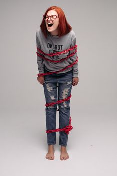 Studio portrait of a girl entangled in a chain. A red-haired woman with brown hair tries to get rid of the chain. The concept of a life-like situation. Isolated on a gray background.