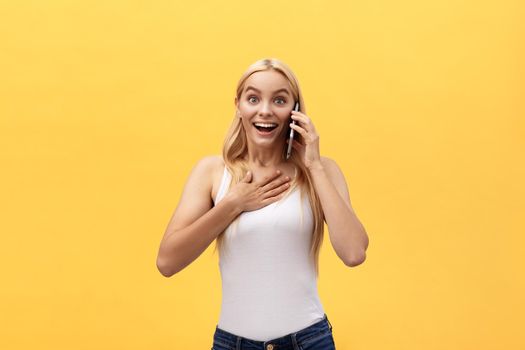 Surprised young woman wearing white clothes while looking at camera isolated on yellow background