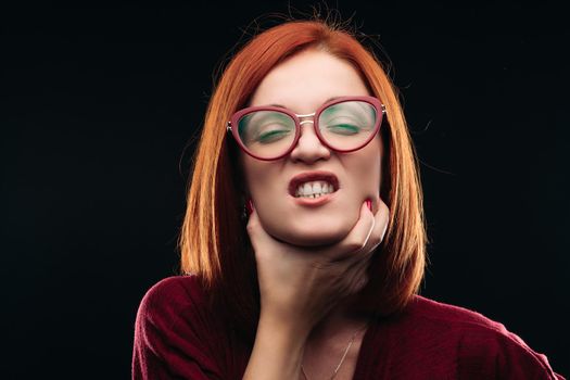 Ill young woman with closed eyes and opened mouth shouting because of her sore throat. Girl with ginger hair having pain in neck or throat. Beautiful model wearing spectacles.