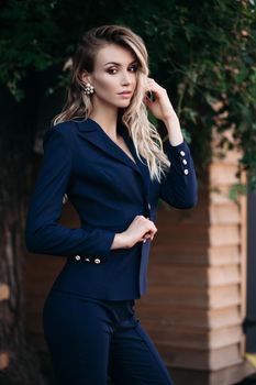 elegant gorgeous blonde businesswoman in expensive dark black jacket and trousers with golden buttons on sleeves. She is standing with arms crossed.