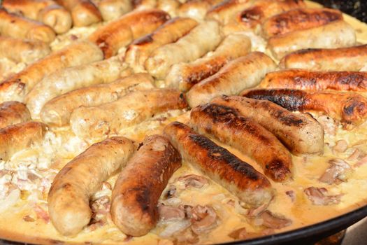 Fried sausages in a large frying pan with mushrooms and white sauce on the market in Paris