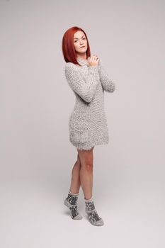 Beautiful and sensuality red haired girl wearing long gray knit sweater and warm socks posing at studio, looking at camera. Comfort and cozy in cold winter evening. Home woman look.