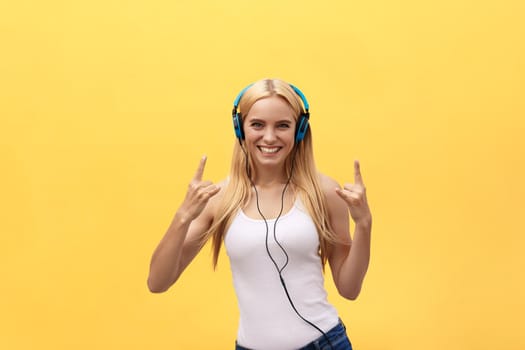 Lifestyle Concept: Portrait of a joyful woman in white t-shirt and listening to music with earphones while dancing and singing isolated over yellow background.