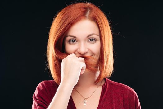 Adorable young woman having straight, ginger short hair. Charming and gorgeous girl satisfied with her trendy haircut. Model holding lock of hair near face and looking at camera.