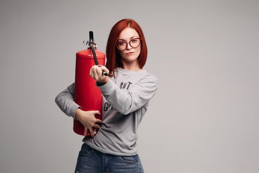 A woman with red hair in the Studio holding a fire extinguisher. An emotional bright woman extinguishes everything with a fire extinguisher