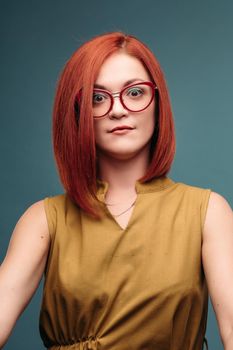 Studio portrait of a happy girl with brown hair. A red-haired woman in stylish glasses smiles looking at the camera. Close-up. Isolated on a blue background