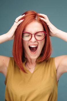 Front view of happy and positivity red haired woman in eyeglasses shouting holding head by hands, looking at camera. Emotionally girl smiling and surprised, having good shock. Drive and happy concept.