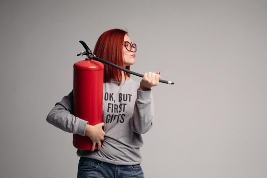 A woman with red hair in the Studio holding a fire extinguisher. An emotional bright woman extinguishes everything with a fire extinguisher