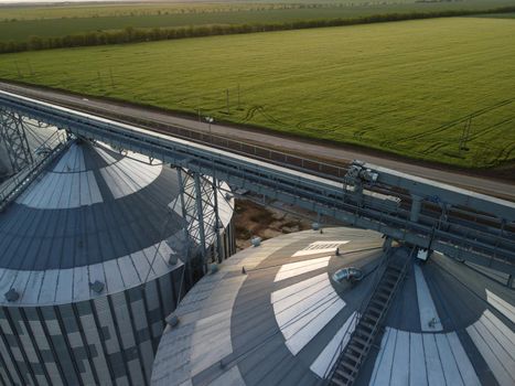 Grain elevator. Metal grain elevator in agricultural zone. Agriculture storage for harvest. Grain silos on green nature background. Exterior of agricultural factory