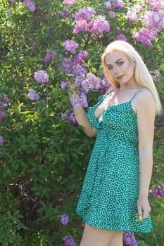 Fashionable girl model near a lilac bush. Spring flowers and beautiful blonde woman. Model appearance. Soft focus