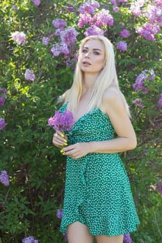 Fashionable girl model near a lilac bush. Spring flowers and beautiful blonde woman. Model appearance. Soft focus