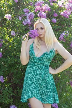 Fashionable girl model near a lilac bush. Spring flowers and beautiful blonde woman. Model appearance. Soft focus