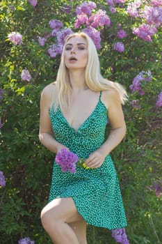 Fashionable girl model near a lilac bush. Spring flowers and beautiful blonde woman. Model appearance. Soft focus