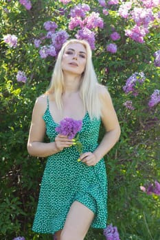 Fashionable girl model near a lilac bush. Spring flowers and beautiful blonde woman. Model appearance. Soft focus