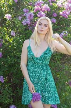 Fashionable girl model near a lilac bush. Spring flowers and beautiful blonde woman. Model appearance. Soft focus