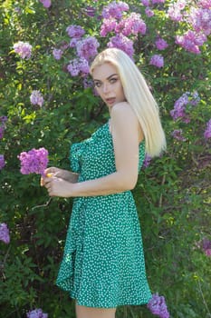 Fashionable girl model near a lilac bush. Spring flowers and beautiful blonde woman. Model appearance. Soft focus