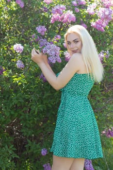 Fashionable girl model near a lilac bush. Spring flowers and beautiful blonde woman. Model appearance. Soft focus