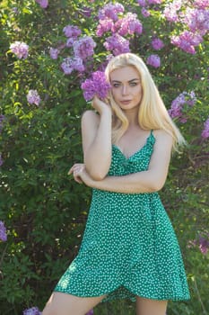 Fashionable girl model near a lilac bush. Spring flowers and beautiful blonde woman. Model appearance. Soft focus