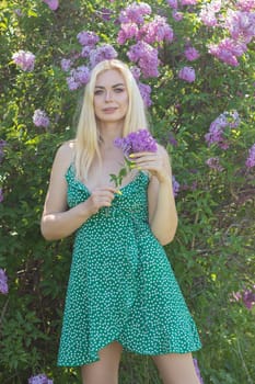 Fashionable girl model near a lilac bush. Spring flowers and beautiful blonde woman. Model appearance. Soft focus