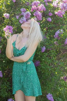 Fashionable girl model near a lilac bush. Spring flowers and beautiful blonde woman. Model appearance. Soft focus