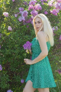 Fashionable girl model near a lilac bush. Spring flowers and beautiful blonde woman. Model appearance. Soft focus