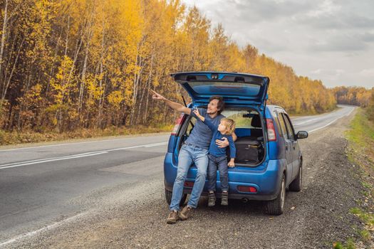 Dad and son are resting on the side of the road on a road trip. Road trip with children concept.