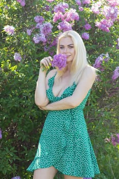 Fashionable girl model near a lilac bush. Spring flowers and beautiful blonde woman. Model appearance. Soft focus