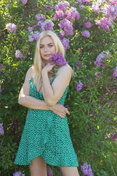 Fashionable girl model near a lilac bush. Spring flowers and beautiful blonde woman. Model appearance. Soft focus