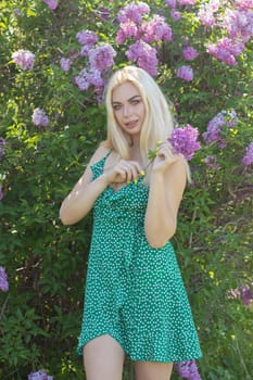 Fashionable girl model near a lilac bush. Spring flowers and beautiful blonde woman. Model appearance. Soft focus