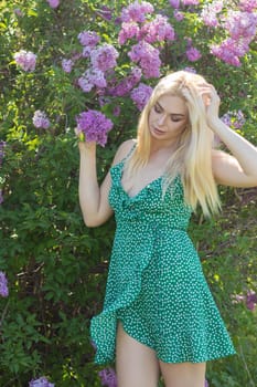 Fashionable girl model near a lilac bush. Spring flowers and beautiful blonde woman. Model appearance. Soft focus