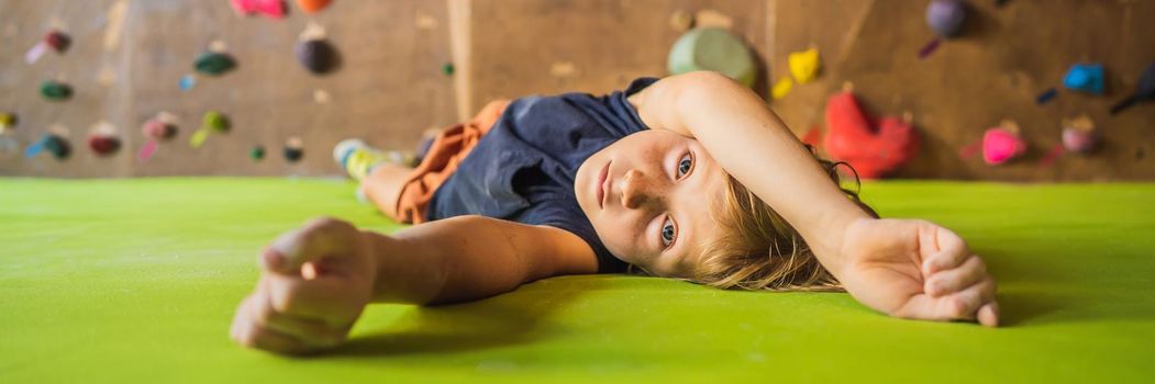 Boy resting after climbing a rock wall indoor. BANNER, LONG FORMAT