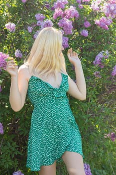 Fashionable girl model near a lilac bush. Spring flowers and beautiful blonde woman. Model appearance. Soft focus