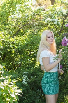 Fashionable girl model near a lilac bush. Spring flowers and beautiful blonde woman. Model appearance. Soft focus