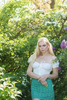 Fashionable girl model near a lilac bush. Spring flowers and beautiful blonde woman. Model appearance. Soft focus