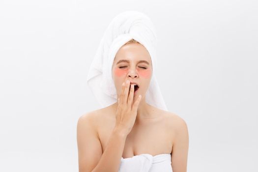 Young beautiful yawning woman with collagen pads under her eyes on a light background. Spa, eye skin care
