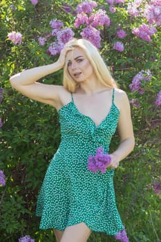 Fashionable girl model near a lilac bush. Spring flowers and beautiful blonde woman. Model appearance. Soft focus