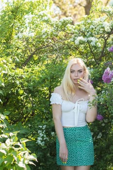 Fashionable girl model near a lilac bush. Spring flowers and beautiful blonde woman. Model appearance. Soft focus