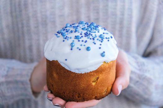 The cook Hands hold Easter cake with white topping and blue sprinkles. Woman holding traditional Russian Easter cake. Homemade pie for spring holiday celebration