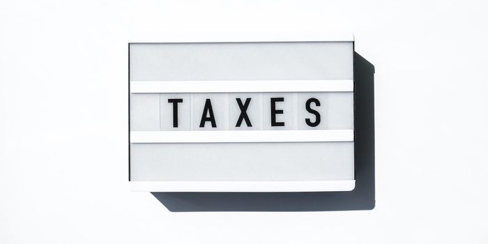 Lightbox board on a white background with the words TAXES in black letters. Currency, cash