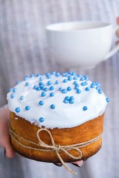 The cook Hands hold Easter cake with white topping and blue sprinkles. Woman holding traditional Russian Easter cake. Homemade pie for spring holiday celebration